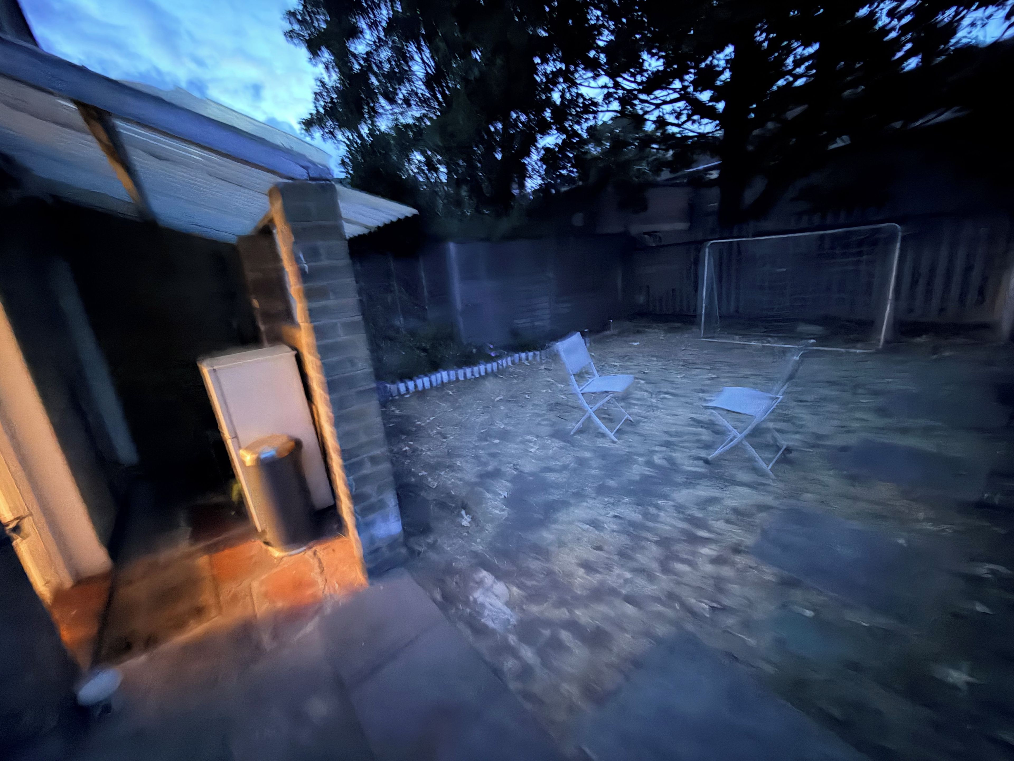 A backyard with a patio area, a white chair, and a small table.