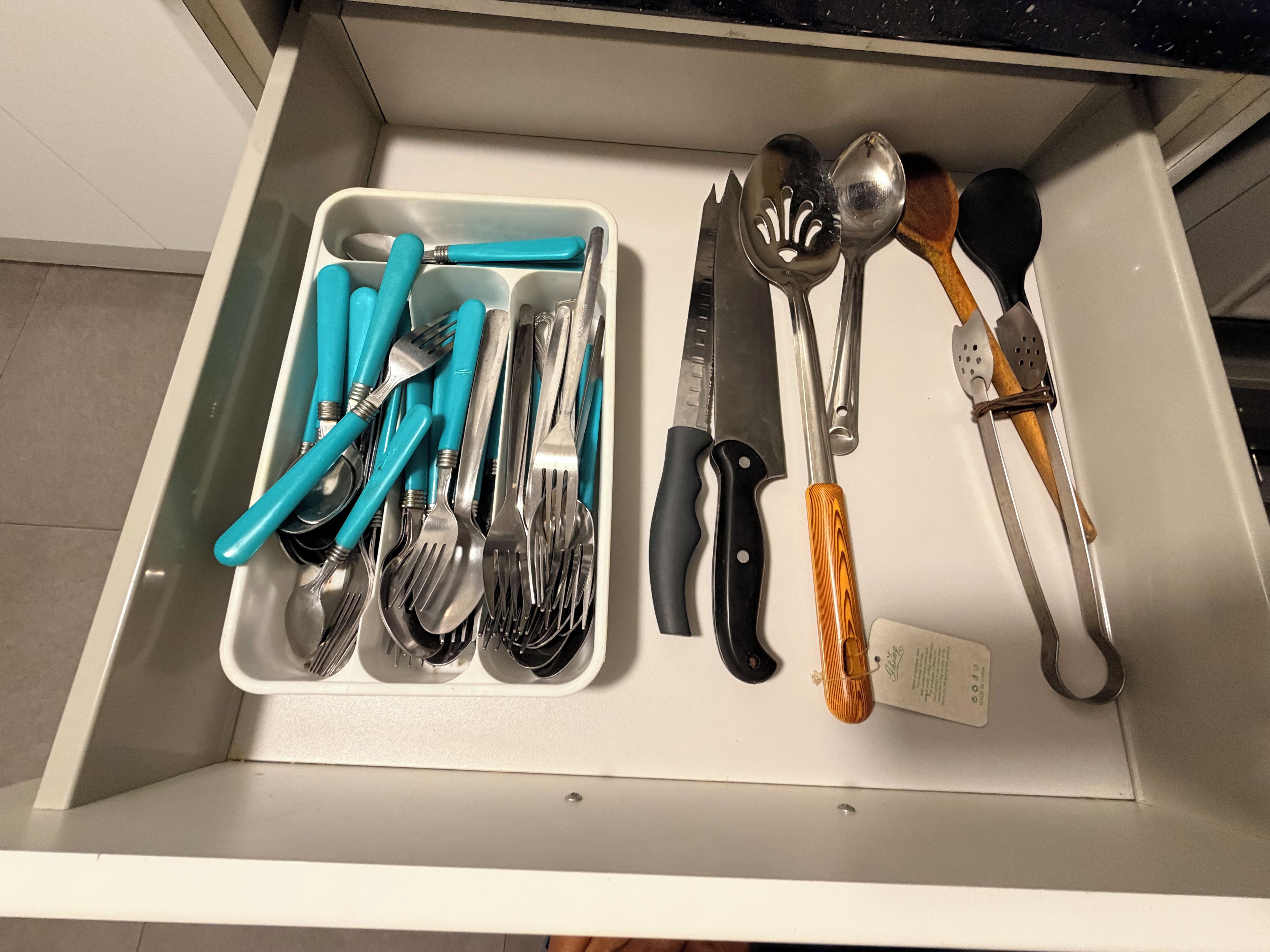 En skuffe med forskellige køkkenredskaber, herunder gafler, knive og skeer.
