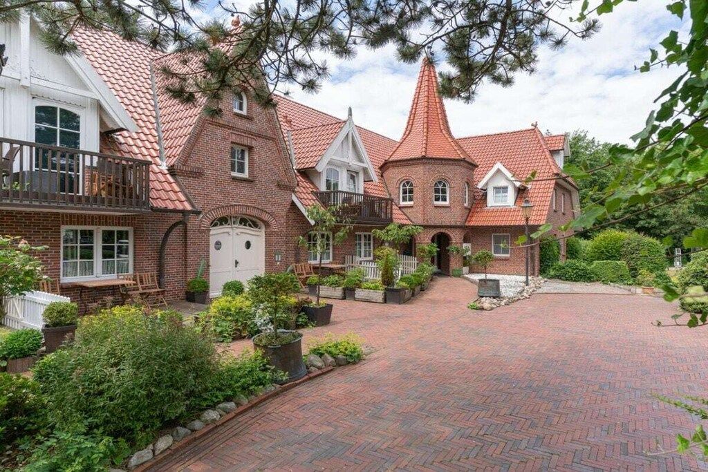 A traditional brick house with a red-tiled roof, a central turret, and a paved driveway.