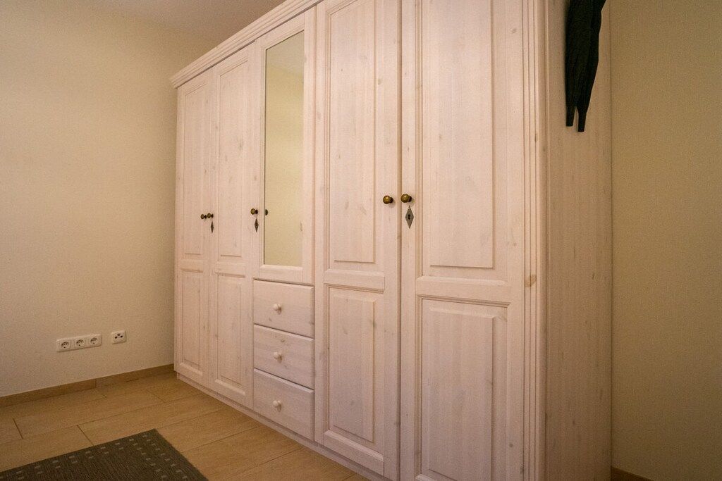 Ein Zimmer mit einem großen weißen Kleiderschrank, einem Spiegel und einem kleinen Teppich.