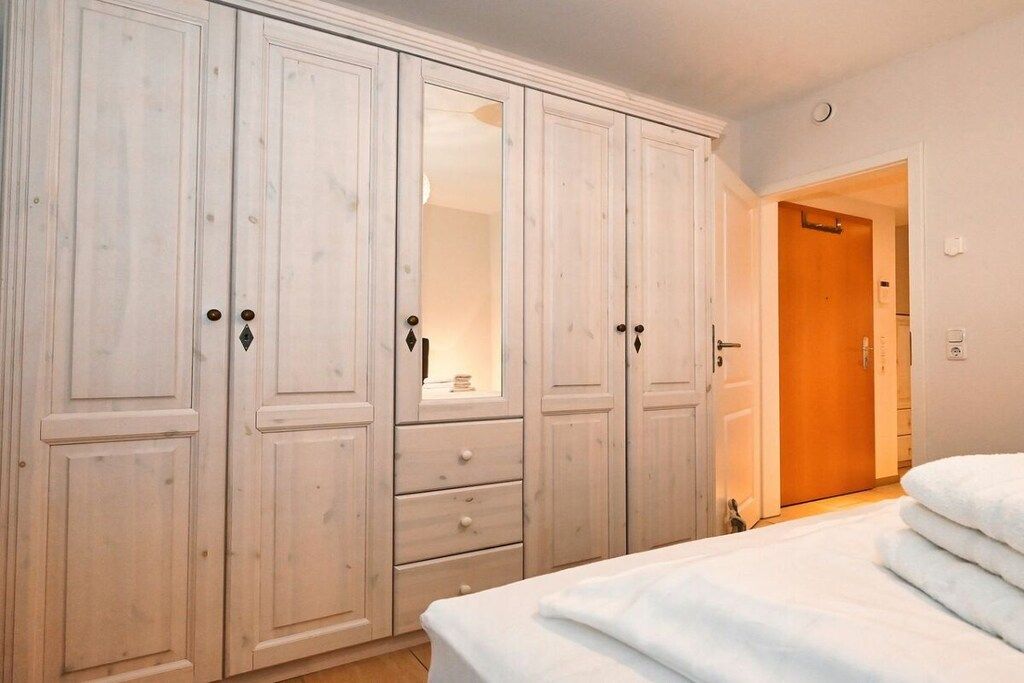 Une chambre dotée d’une grande armoire, d’un lit avec une literie blanche et d’une porte donnant sur une autre pièce.