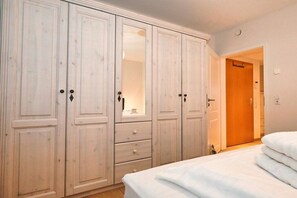 A bedroom with a large wardrobe, a bed with white bedding, and a door leading to another room. - Holiday apartment in Büsum with swimming pool (Büsum)