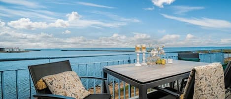 An outdoor dining area with a view of the sea, a table set with candles, and chairs with patterned cushions.