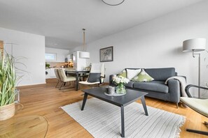 Ein modernes Wohnzimmer mit einem grauen Sofa, einem Couchtisch und einem Essbereich im Hintergrund.