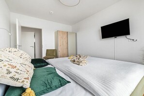Ein Schlafzimmer mit einem Bett, einem an der Wand montierten Fernseher und einer Tür zu einem weiteren Raum.