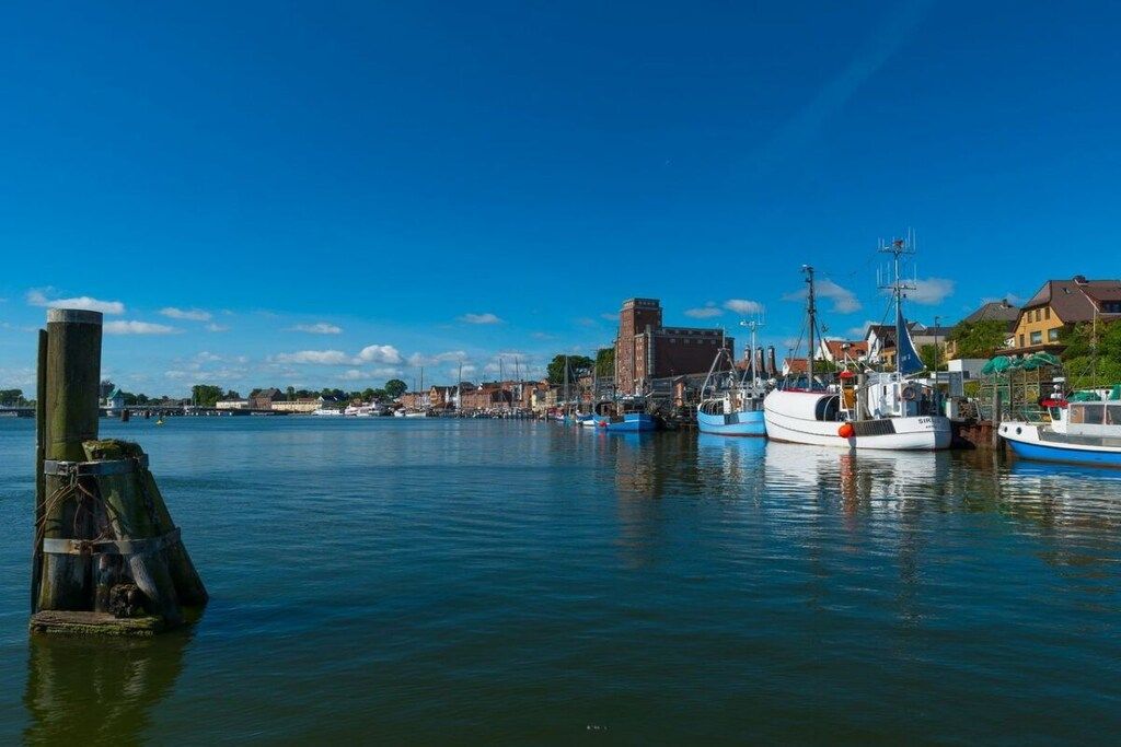A harbor with boats docked, a prominent lighthouse, and buildings along the waterfront.