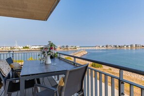 A terrace with a table and chairs, overlooking a body of water and a distant shoreline. - Apartment in Olpenitz with swimming pool (Olpenitz)