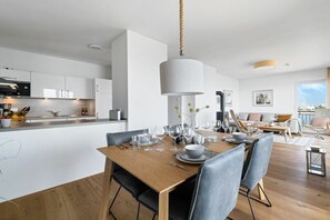 A modern kitchen with white cabinetry, a dining area with a wooden table set for four, and a living space with a sofa and chairs. - Apartment in Olpenitz with swimming pool (Olpenitz)