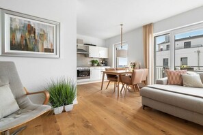 Ein modernes Wohnzimmer mit einer Couch, einem Esstisch mit Stühlen, einer Küche im Hintergrund und einem großen Fenster mit Blick.