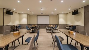 Un salón de conferencias con una pantalla grande, varias mesas y sillas.