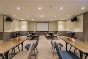 Uma sala de conferências com uma tela grande, várias mesas e cadeiras.
