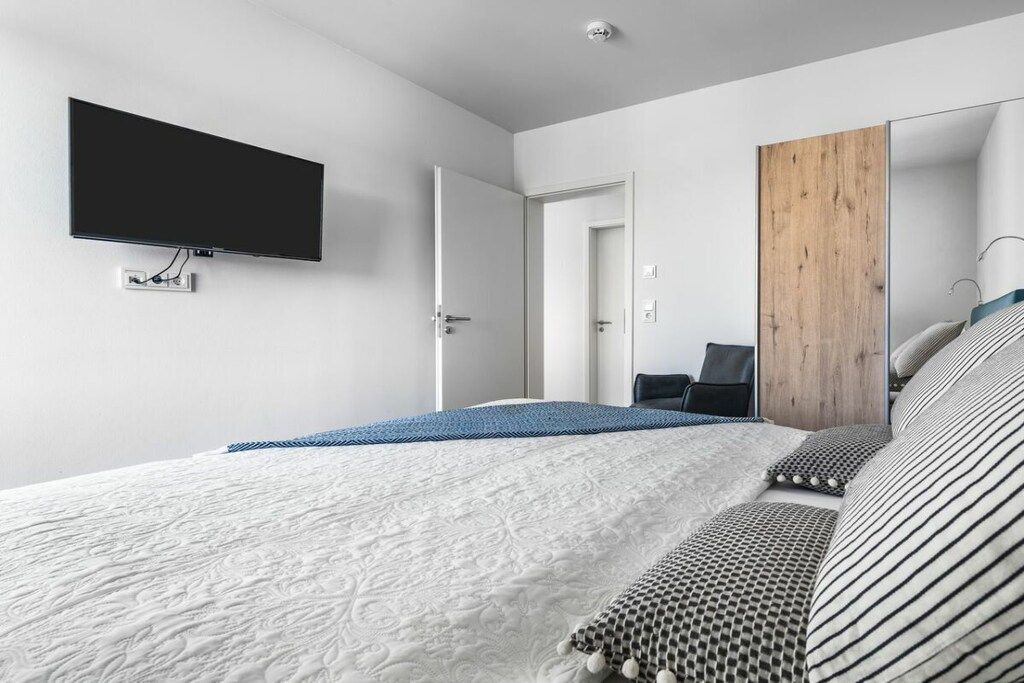 Quarto moderno com televisão de tela plana na parede, cama com roupa de cama estampada, guarda-roupa de madeira e um espelho.