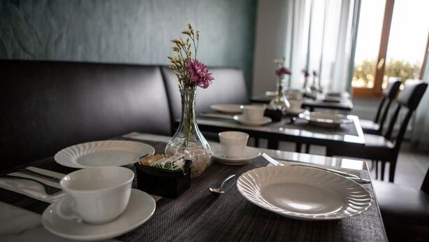 A dining table set with white plates, cups, and cutlery, a vase with flowers, and a small box of tissues.