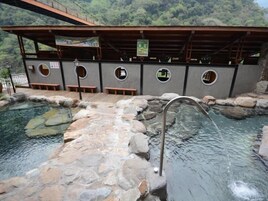 A traditional Japanese onsen with stone baths, wooden benches, and a wooden structure with a roof.
