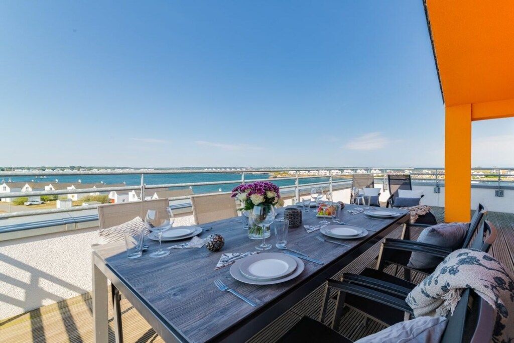 A dining table set for two with a view of the sea and a distant bridge.