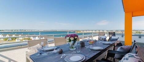 A dining table set for two with a view of the sea and a distant bridge.
