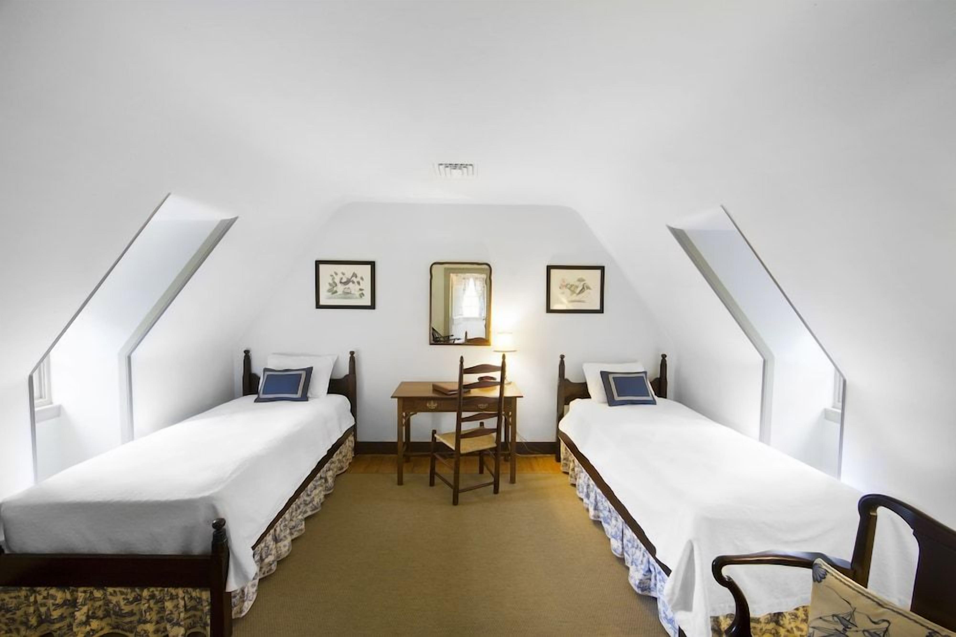 A room with two single beds, a desk, and a chair.