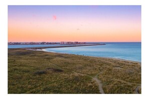 Un paysage côtier avec un ciel dégagé, une plage de sable et une silhouette de ville visible au loin.