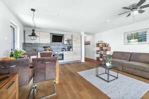 A modern kitchen with a flat-screen TV, wooden cabinets, and a dining area with leather chairs. - Holiday apartment with 1 bedroom (Kappeln)