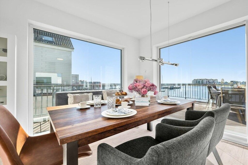 A dining area with a wooden table, grey upholstered chairs, and a view of the city through large windows.