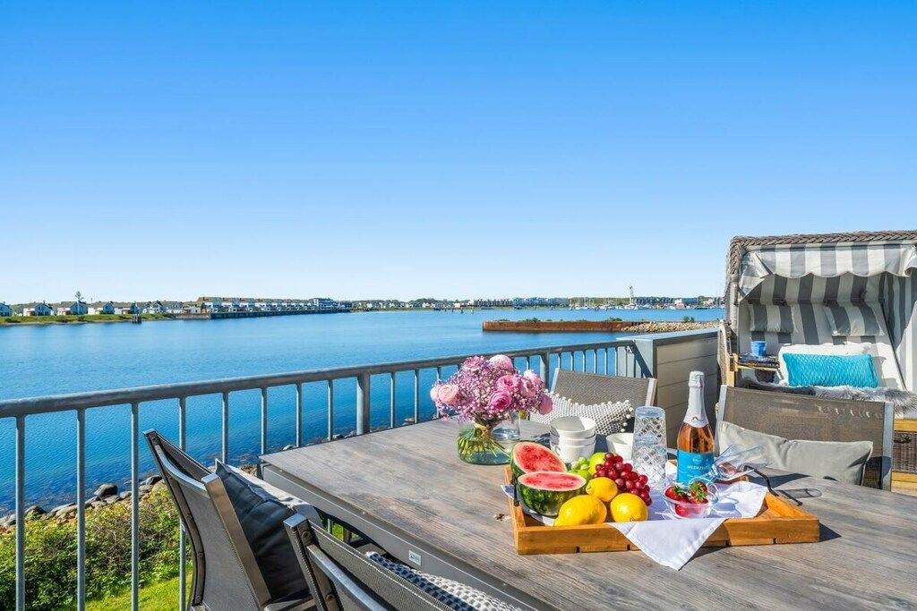 A dining area with a table set for a meal, overlooking a body of water with a distant shoreline.