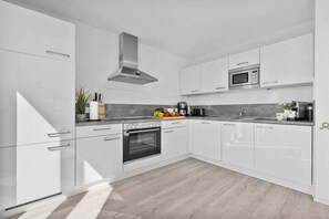 A modern kitchen with white cabinetry, a stainless steel range hood, a microwave, and a built-in oven. - Holiday apartment with 1 bedroom (Kappeln)