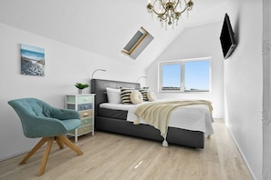 A bedroom with a bed, a chair, a bedside table, a TV, and a window. - Holiday apartment with 1 bedroom (Kappeln)