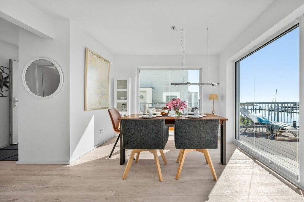 Un espace de repas moderne avec une table et des chaises en bois, une grande fenêtre et une vue sur le balcon.