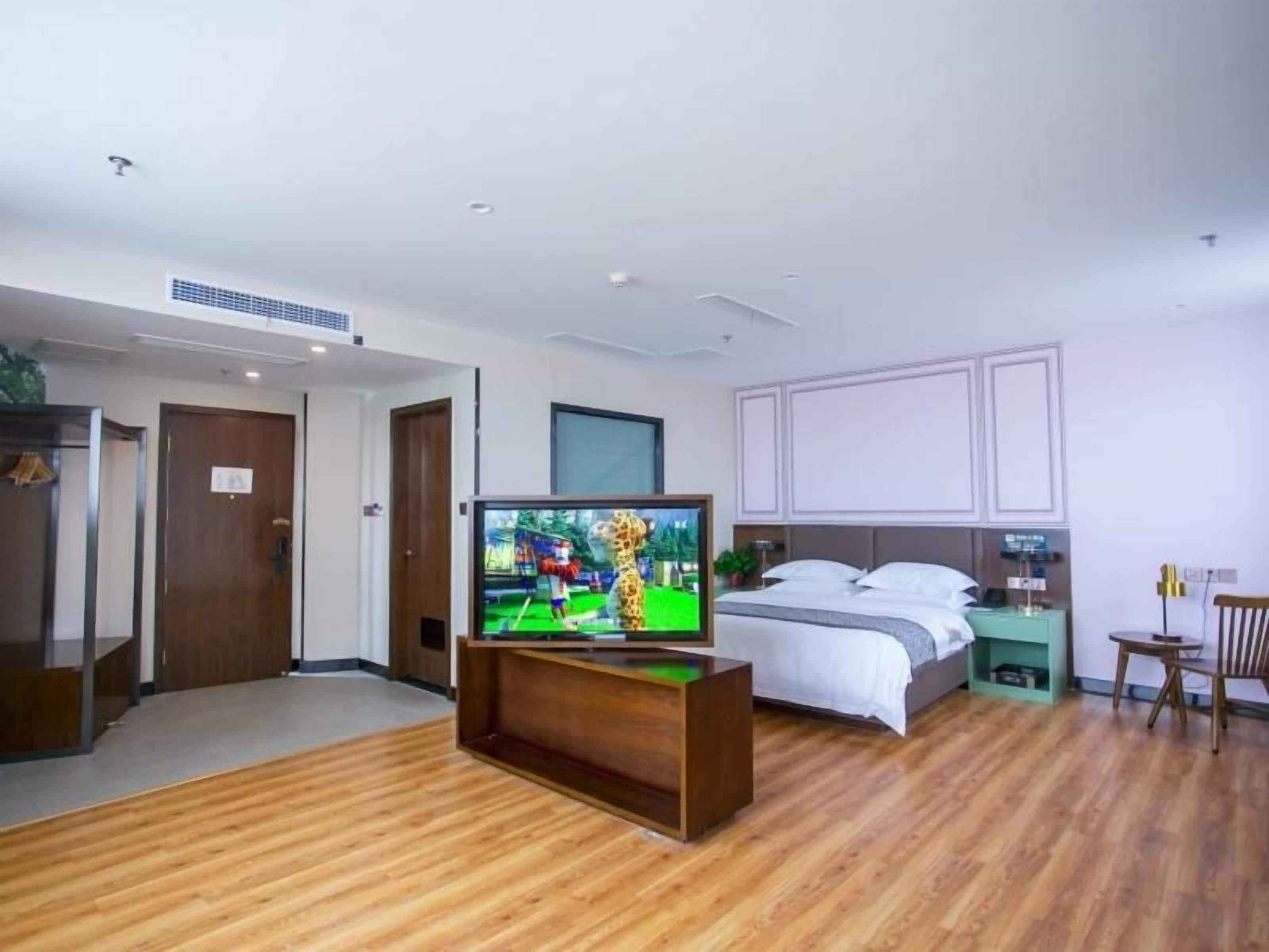 Ein Hotelzimmer mit Holzboden, einem Bett mit weißer Bettwäsche, einem Fernseher auf einem Holzbodenständchen und einem Nachttisch mit Lampe.