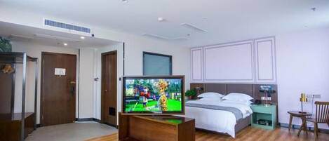 Ein Hotelzimmer mit Holzboden, einem Bett mit weißer Bettwäsche, einem Fernseher auf einem Holzbodenständchen und einem Nachttisch mit Lampe.