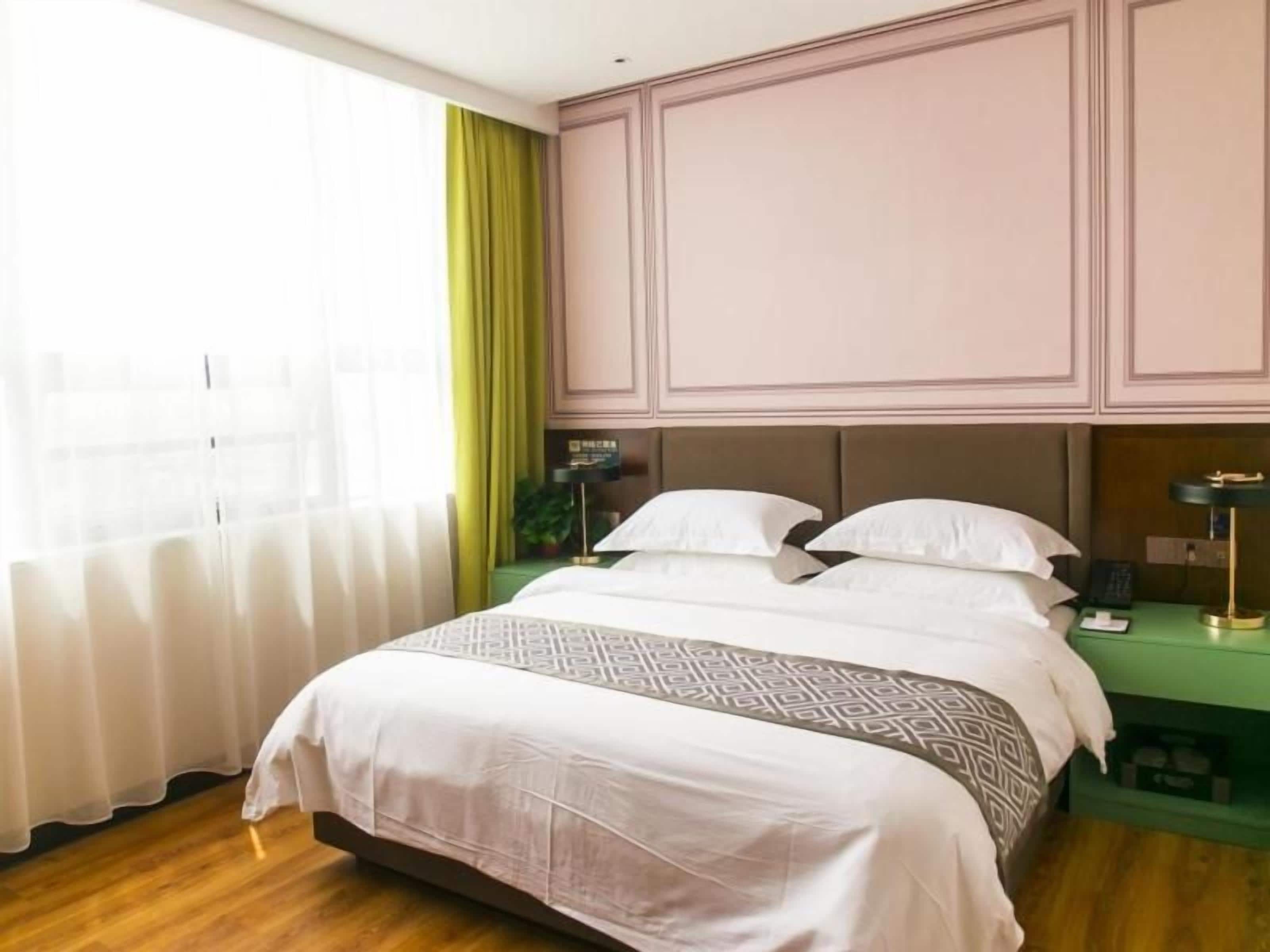 A hotel room with a bed, bedside tables, a nightstand, a lamp, and a window with curtains.
