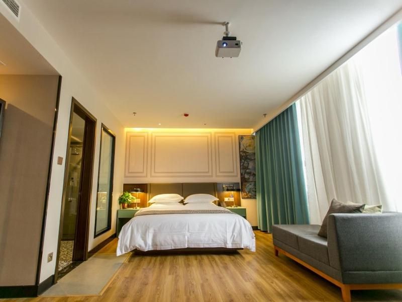 Una habitación de hotel con cama, sofá, proyector y ventana con cortinas.
