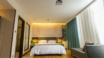 Una habitación de hotel con cama, sofá, proyector y ventana con cortinas.