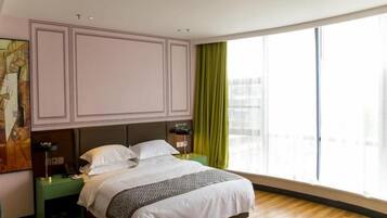 Un dormitorio con una cama grande, una mesita de noche, una lámpara y vistas a la ciudad a través de amplias ventanas.