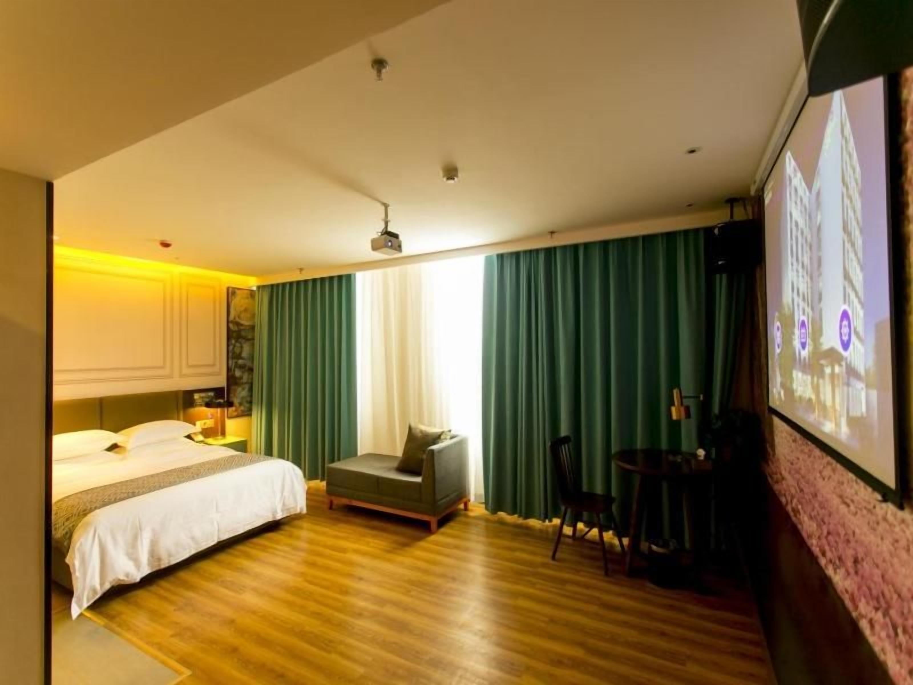 Quarto de hotel com cama, área de estar, escrivaninha e uma televisão grande.
