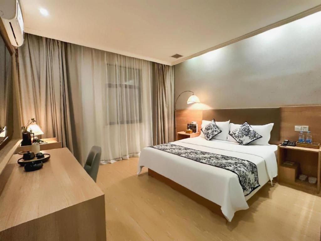 A hotel room with a bed, bedside tables, a desk, and a lamp.