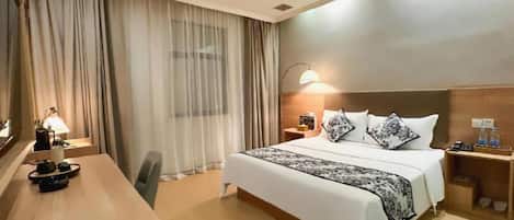 A hotel room with a bed, bedside tables, a desk, and a lamp.