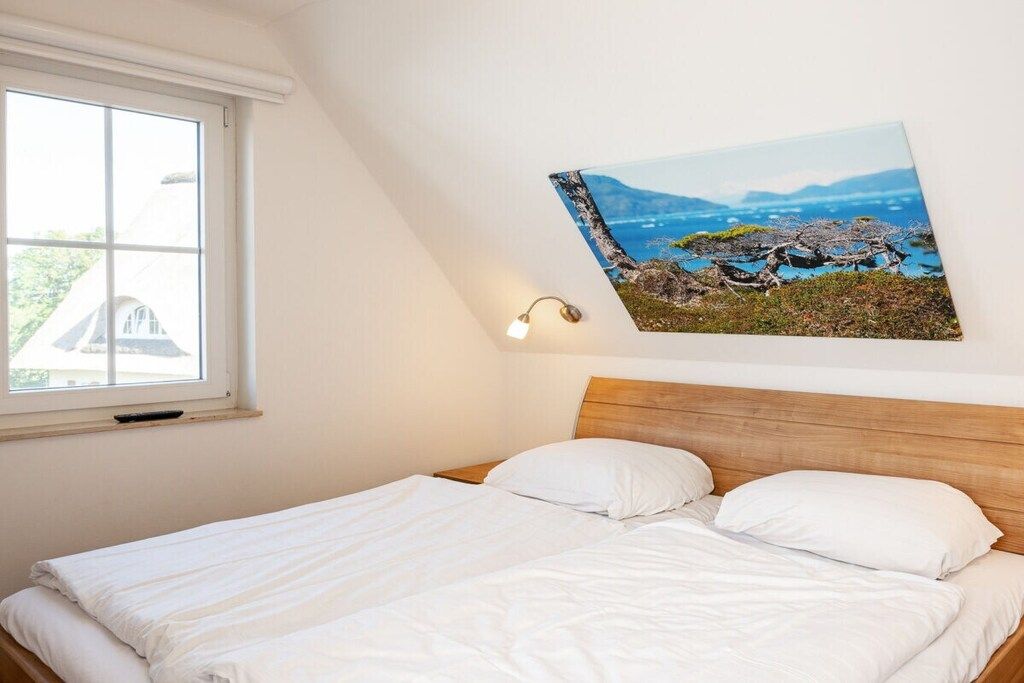 A bedroom with a bed, a window, and a wall-mounted picture.