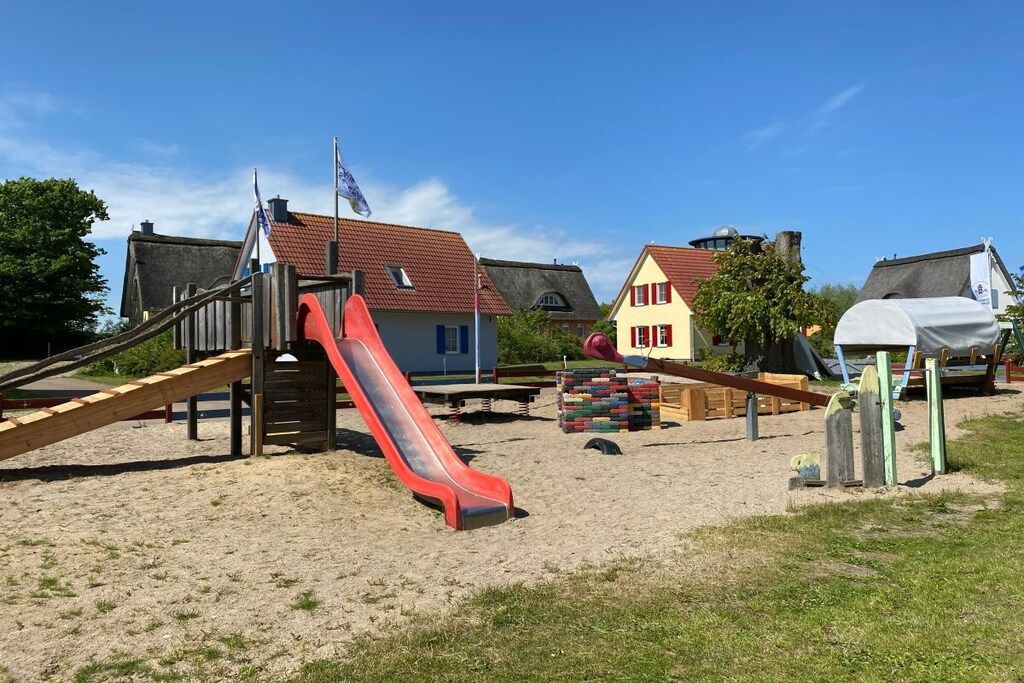 A playground with a red slide, sand, and a small building with a red roof.