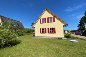 A two-story house with a red roof and white shutters, surrounded by a well-maintained lawn and neighboring houses. - Holiday home with 1 bedroom (Hohenkirchen Wohlenberger Wiek)
