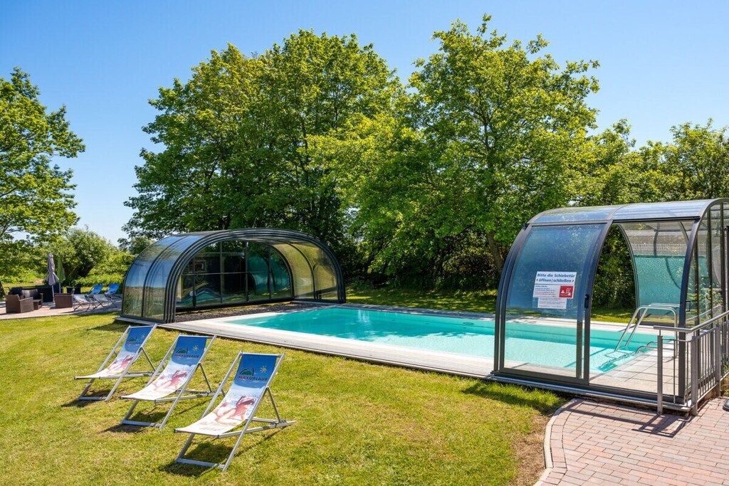 A swimming pool with a glass enclosure, surrounded by grass and trees.