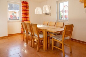 A dining area with a wooden table and chairs, two pendant lights, and a view through the window. - Holiday home with 1 bedroom (Hohenkirchen Wohlenberger Wiek)