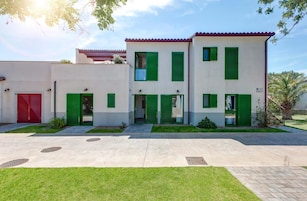 Un edificio moderno de dos pisos con contraventanas verdes, una puerta de garaje roja y un césped bien cuidado.