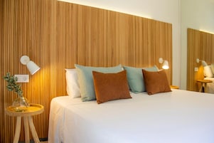 Habitación de hotel con una cama, almohadas, lámparas de noche, una mesita con una planta y un espejo en la pared.