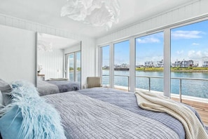 Ein Schlafzimmer mit einem großen Bett, einem Sessel und Blick auf ein Gewässer durch große Fenster.