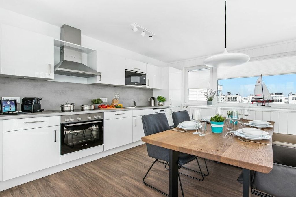 A modern kitchen with white cabinetry, a wooden dining table, and a view of the city.