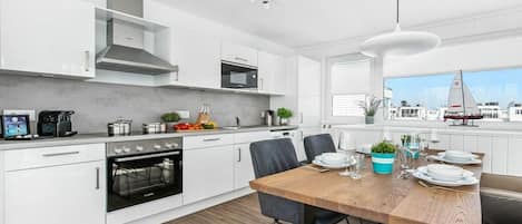 A modern kitchen with white cabinetry, a wooden dining table, and a view of the city.