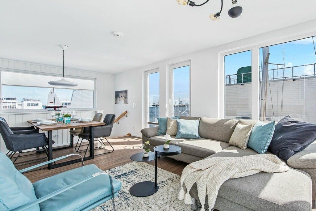 Ein modernes Wohnzimmer mit einer Couch, Sesseln, einem Esstisch und Blick auf die Stadt durch große Fenster.