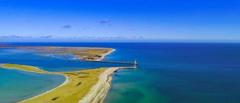 An aerial view of a coastal area with a lighthouse, clear blue waters, and a sandy beach.