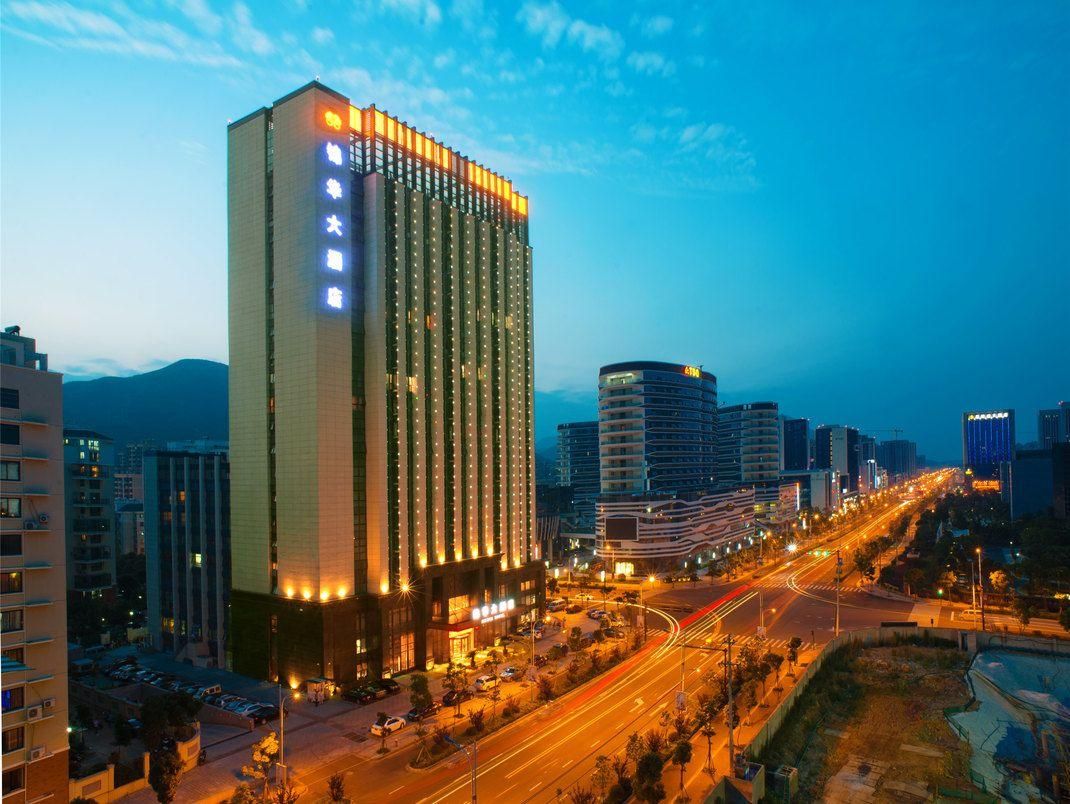A high-rise hotel with multiple floors, a parking area, and a busy road with light trails indicating traffic.